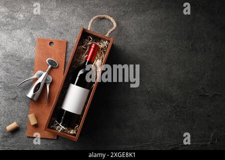 Bouteille de vin dans une boîte en bois, bouchons et tire-bouchon sur une table texturée sombre, pose à plat. Espace pour le texte Banque D'Images