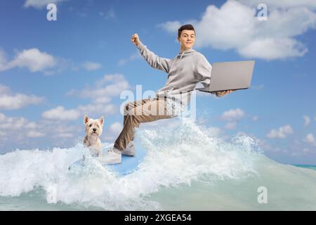 Adolescent mâle avec un chien surfant sur une vague et tenant un ordinateur portable dans la mer Banque D'Images