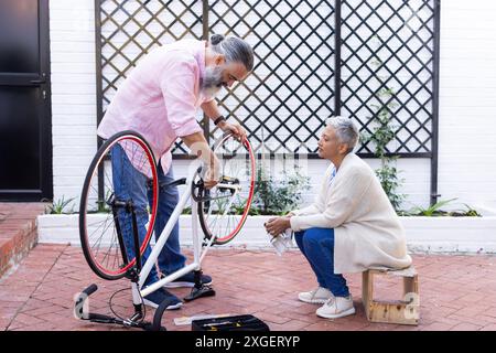 Réparation du vélo, homme senior fixant le vélo tandis que la femme est assise et regarde Banque D'Images