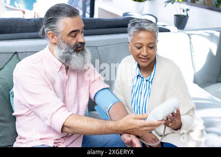 Vérification de la pression artérielle, couple senior assis sur le canapé, se concentrant sur la santé Banque D'Images