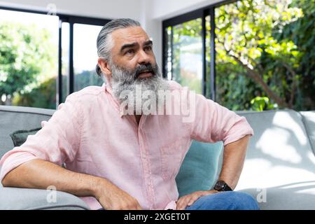 Assis sur le canapé, homme senior avec la barbe regardant réfléchi dans le salon Banque D'Images