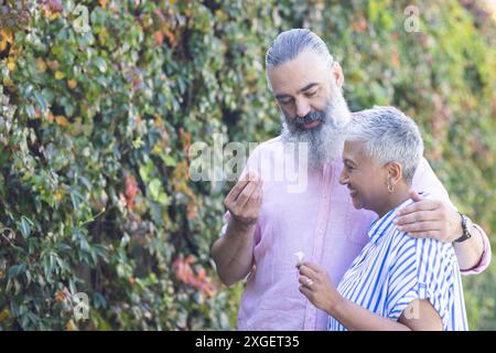Couple senior appréciant la promenade dans la nature, souriant et tenant des fleurs ensemble, copiez l'espace Banque D'Images