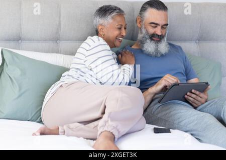 Couple senior se relaxant sur le lit, en utilisant la tablette et en souriant ensemble Banque D'Images