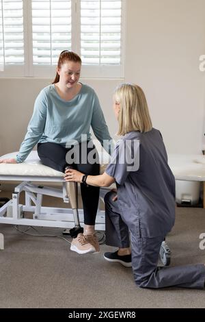 Thérapeute ajustant la jambe prothétique d'une femme assise sur une table d'examen Banque D'Images