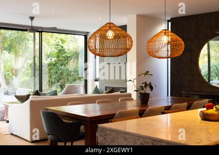 Salle à manger moderne avec table en bois et suspensions en osier dans une maison confortable, espace copie Banque D'Images