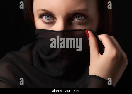 Portrait en gros plan extrême d'une femme couvrant son nez et sa bouche avec un foulard noir et regardant dans la caméra. Femme adulte caucasienne avec gris frappant Banque D'Images