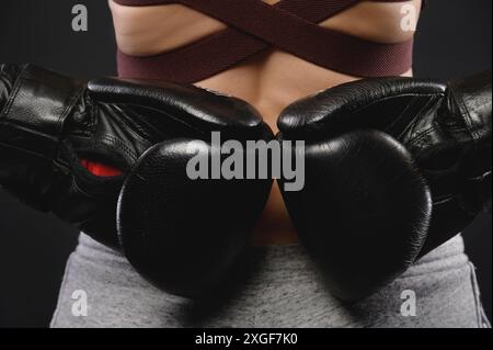 Gros plan à partir de l'arrière de la main d'une femme athlète en gants de boxe noirs. Concept de la force de la femme et de la lutte féminine Banque D'Images