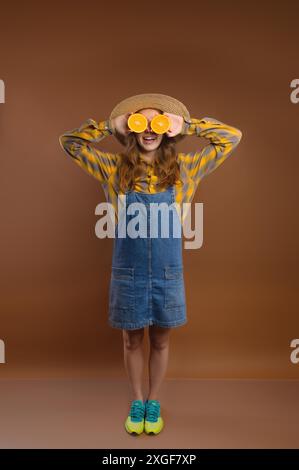 Portrait studio d'une femme hipster joyeuse devenant folle faisant un visage drôle et couvrant ses yeux avec des oranges Banque D'Images