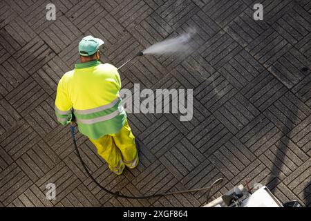 Un travailleur nettoie un trottoir de rue avec une machine à jet d'eau haute pression le jour ensoleillé. Copier l'espace. Vue de dessus Banque D'Images