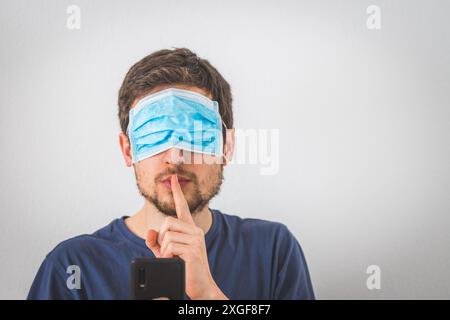 Jeune homme en colère avec masque facial sur les yeux fait un psst! geste Banque D'Images