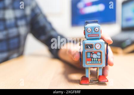 Robot jouet sur un bureau, homme travaillant sur l'ordinateur en arrière-plan. Symbole de l'intelligence artificielle, des chatbots ou des bots sociaux et des algorithmes Banque D'Images