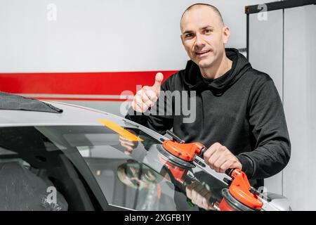 Technicien automobile travailleur remplaçant le pare-brise ou le pare-brise d'une voiture dans le garage de la station-service automobile. Photo de haute qualité Banque D'Images