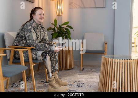 Assise dans la salle d'attente, femme en uniforme indéfini avec une jambe prothétique souriante, espace de copie Banque D'Images