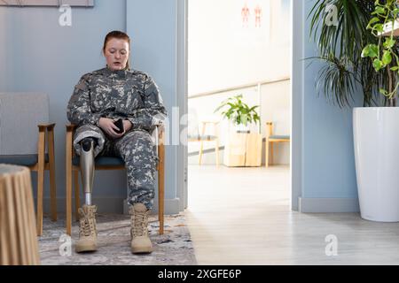 Dans la salle d'attente, femme en uniforme indéfini avec une jambe prothétique à l'aide d'un smartphone, espace de copie Banque D'Images