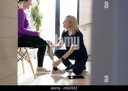 Pose de jambe prothétique, femme aidant une patiente dans un établissement médical moderne Banque D'Images