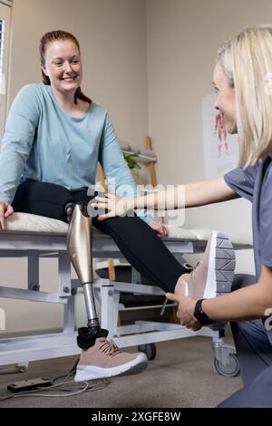 Femme avec une jambe prothétique souriante alors que le thérapeute l'ajuste en clinique Banque D'Images