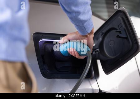 Charge voiture électrique, personne branchant le chargeur à la station d'accueil Banque D'Images