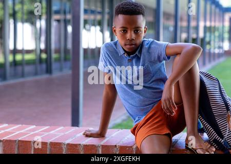 Portrait d'un écolier afro-américain sérieux assis sur le mur à l'extérieur de l'école, avec espace de copie Banque D'Images