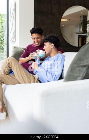 Détente sur le canapé, couple gay masculin appréciant le café et souriant l'un à l'autre Banque D'Images