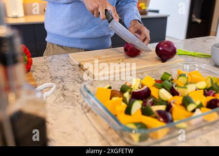 Hacher des légumes sur une planche à découper, homme préparant le repas dans la cuisine Banque D'Images