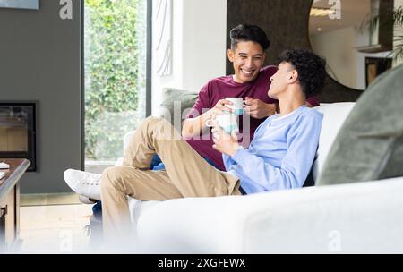 Détente sur le canapé, couple gay masculin appréciant le café et souriant à la maison Banque D'Images