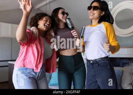 Chanter karaoké, trois femmes amies s'amusant avec des microphones à la fête à la maison Banque D'Images