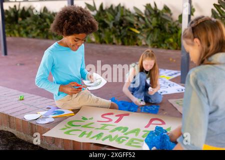 Heureux et divers écoliers faisant des affiches d'écologie pendant la classe d'art de l'école en plein air Banque D'Images