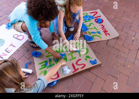 Heureux et divers écoliers faisant des affiches d'écologie pendant la classe d'art de l'école en plein air Banque D'Images