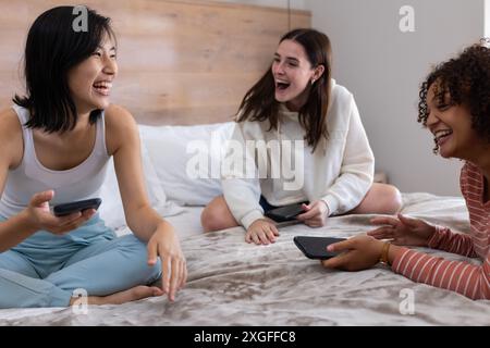 Rire et bavarder, trois amies assises au lit avec des smartphones Banque D'Images