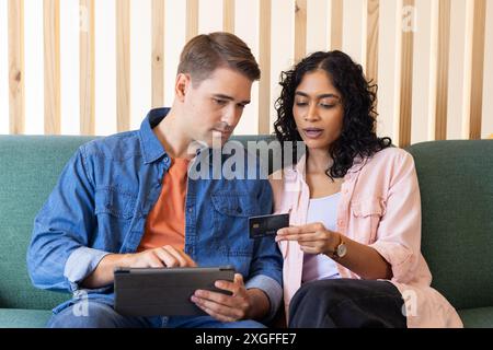 En utilisant la tablette, jeune couple effectuant le paiement en ligne avec la carte de crédit sur le canapé Banque D'Images