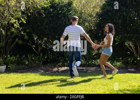 Jeune couple tenant la main et courant ensemble dans le jardin ensoleillé, espace de copie Banque D'Images