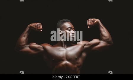 Homme musclé Flexing biceps sur fond noir Banque D'Images