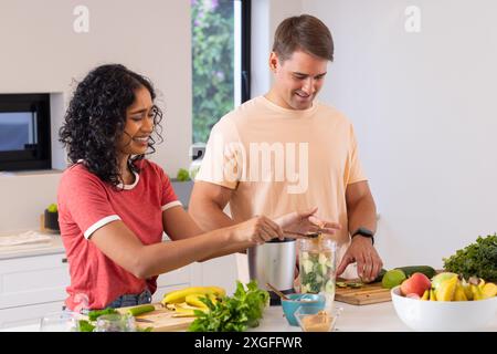 Préparer un smoothie sain, jeune couple hachant des fruits dans la cuisine Banque D'Images