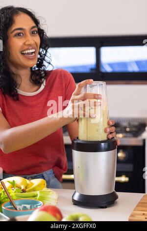 Faire smoothie, femme mélangeant des fruits frais dans la cuisine, souriant et heureux Banque D'Images