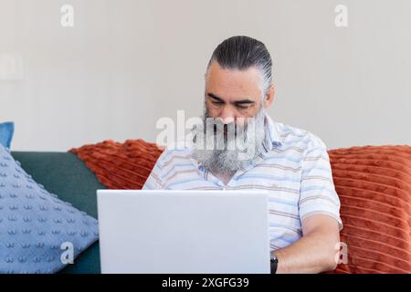 Travaillant à la maison, homme âgé utilisant un ordinateur portable tout en étant assis sur le canapé Banque D'Images