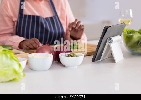 Hacher des légumes, personne suivant la recette sur tablette dans la cuisine moderne Banque D'Images