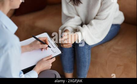 Psychologue méconnaissable parlant avec le client prenant des notes assis au bureau Banque D'Images