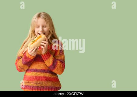 Mignonne petite fille mangeant hot dog savoureux sur fond vert Banque D'Images