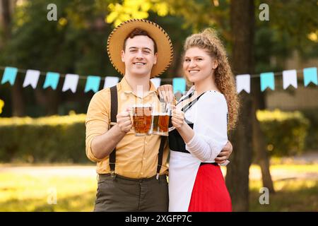 Jeune couple en vêtements traditionnels allemands avec de la bière célébrant Octoberfest en plein air Banque D'Images