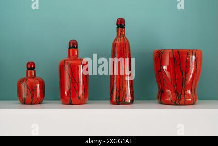 Quatre verres de Murano rouges avec des rayures noires se tiennent sur l'étagère blanche Banque D'Images