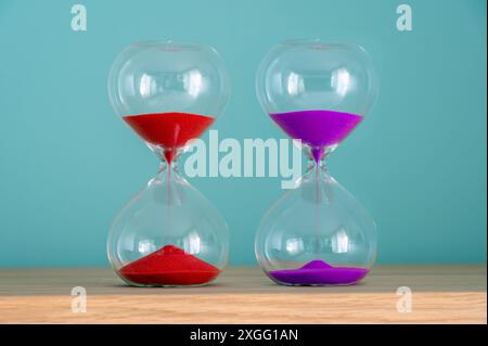 Deux sabliers colorés debout sur une surface en bois montrent le temps qui passe Banque D'Images