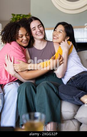 Trois femmes amies embrassant et souriant, profitant du temps ensemble sur le canapé à la maison Banque D'Images