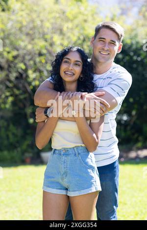 Jeune couple souriant embrassant à l'extérieur dans un jardin ensoleillé, profitant du temps ensemble Banque D'Images