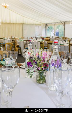 tables avec des verres et des fleurs installées dans un chapiteau pour une fête Banque D'Images