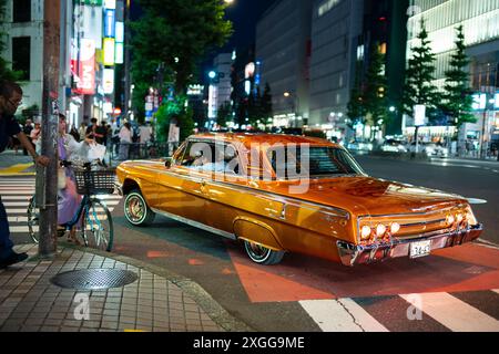 Tokyo, Japon - 16 juin 2024 : une automobile américaine vintage, peinte en orange, est conduite dans les rues de Tokyo la nuit pendant une soirée d'été. Banque D'Images