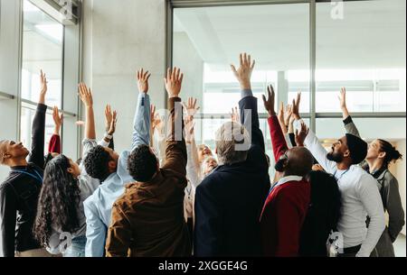 Groupe diversifié de personnes montrant l'excitation et le travail d'équipe en levant la main lors d'un séminaire d'affaires dans un environnement de bureau moderne. Banque D'Images