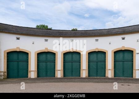 Quatre grandes portes vertes sont aménagées dans un bâtiment blanc incurvé. Les portes sont cintrées et ont des détails décoratifs. Il y a de petites fenêtres au-dessus de chaque porte et un toit en ardoise. Banque D'Images