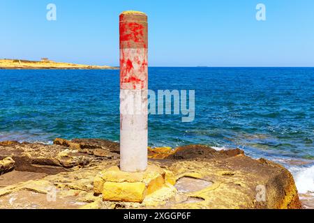 Poste rouge sur une plage rocheuse à côté de l'océan. Pilier se distingue contre l'eau bleue. Vagues de l'océan qui rochent doucement sur les rochers Banque D'Images