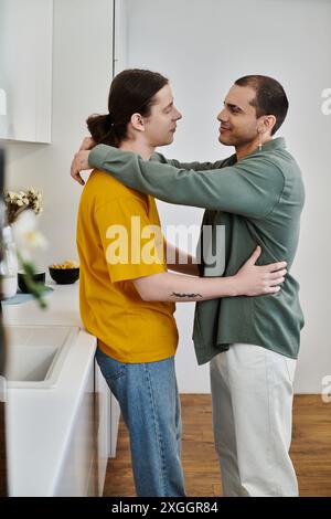 Un jeune couple gay s'embrasse dans leur cuisine moderne, mettant en valeur leur amour et leur connexion. Banque D'Images