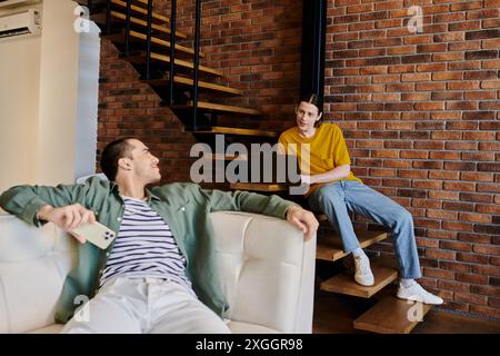 Un jeune couple gay se détend dans leur appartement loft moderne, profitant de la compagnie des autres. Banque D'Images
